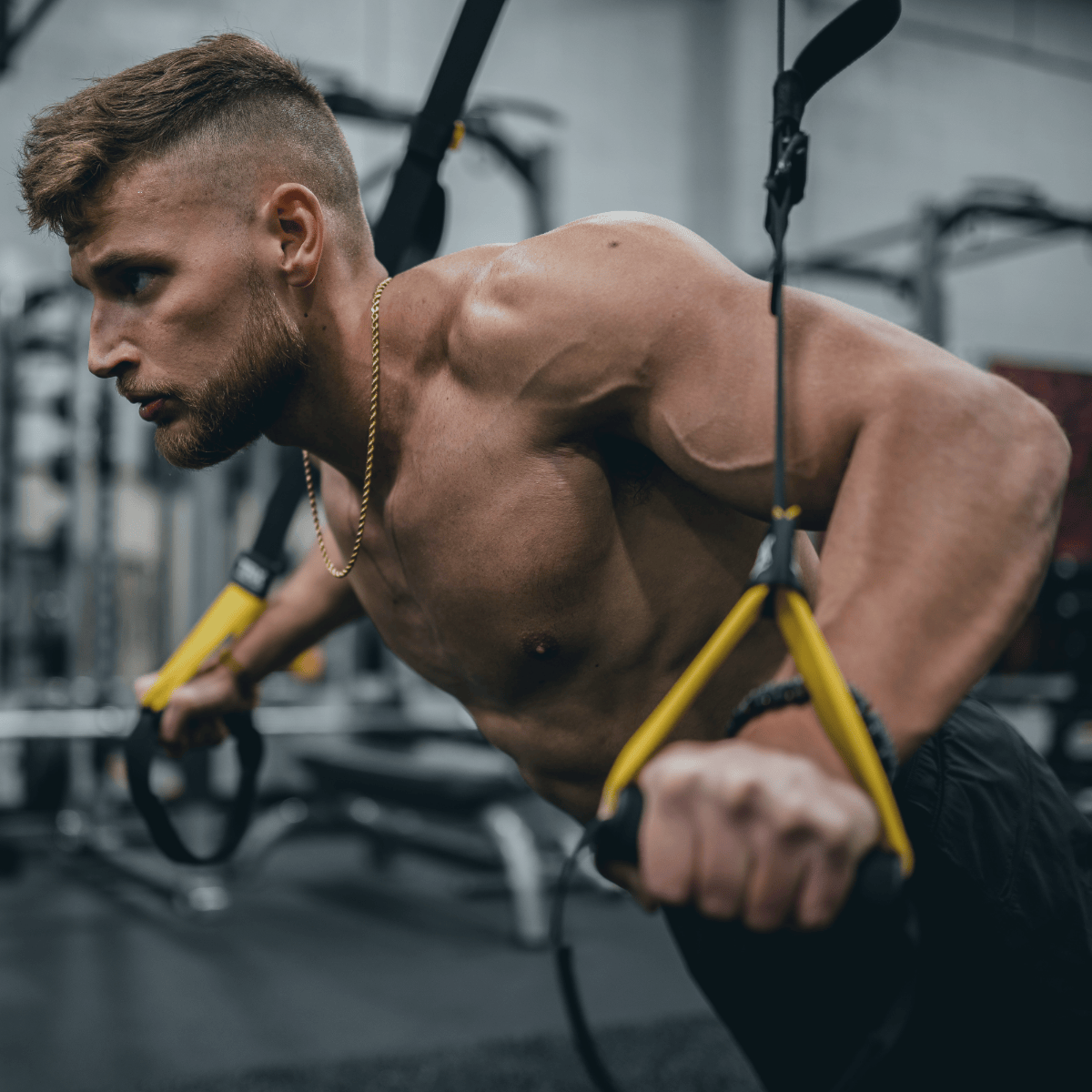 Muscular man exercising with TRX straps in a gym setting