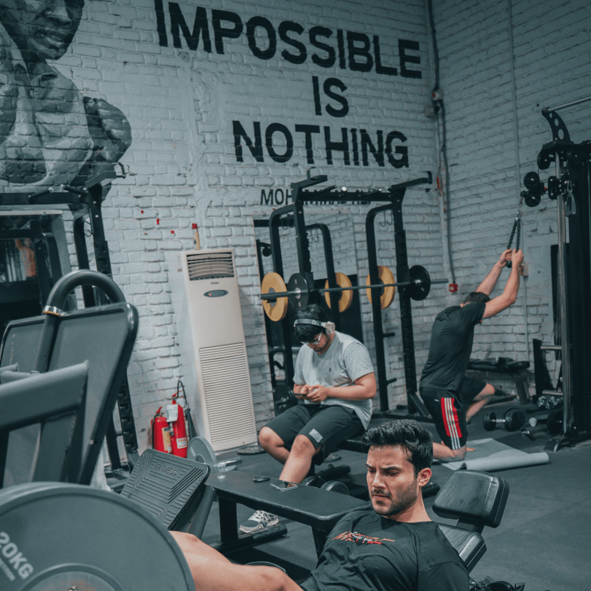Gym interior with motivational quote 'Impossible is Nothing' on wall, people exercising.